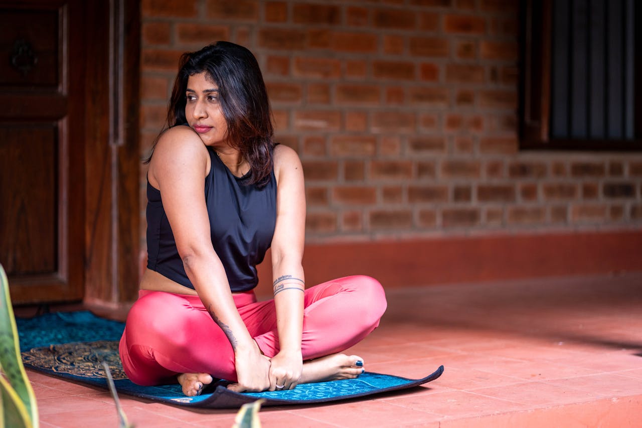 Young woman sitting on a yoga mat outdoors, dressed in vibrant workout gear.