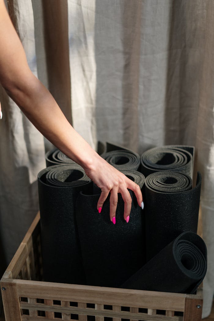 Close-up of a hand selecting a yoga mat from a basket in a yoga studio.